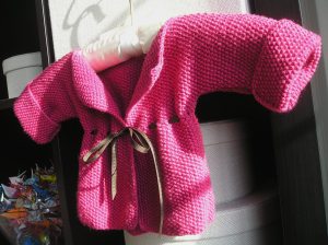"Baby Cardigan" finished, with ribbon, and photographed at a rakish angle